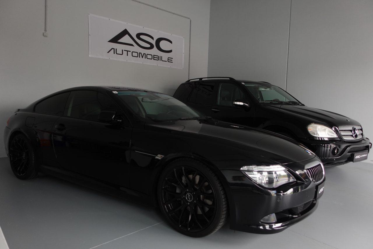 Zwei schwarze Fahrzeuge im Showroom von ASC Automobile: ein BMW Coupé auf schwarzen Felgen, dahinter ein Mercedes SUV