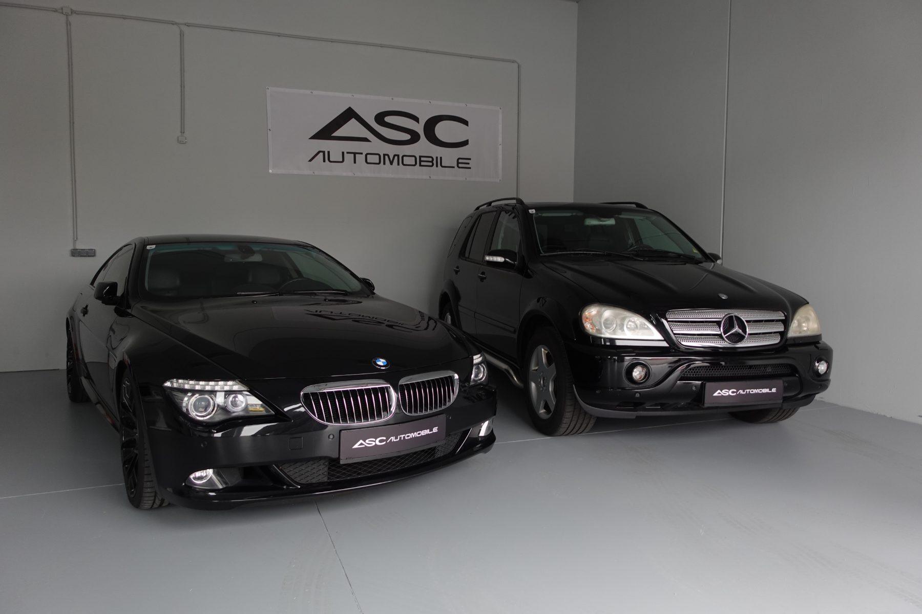 Showroom von ASC Automobile: ein schwarzes BMW Coupé und ein schwarzer Mercedes SUV vor dem ASC-Banner an der Wand