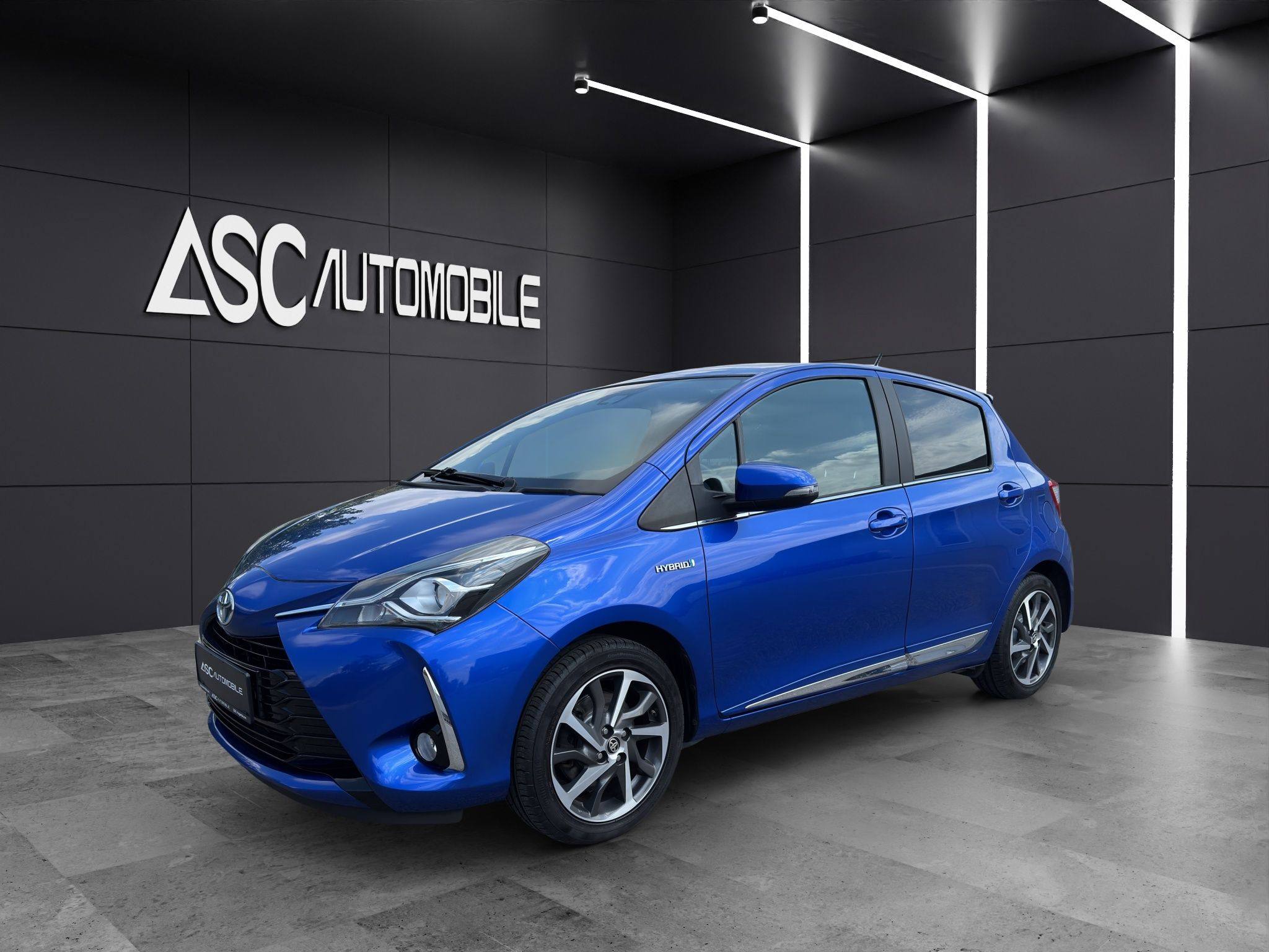 Toyota Yaris Hybrid in Blau, schräg von vorne links im Showroom von ASC Automobile